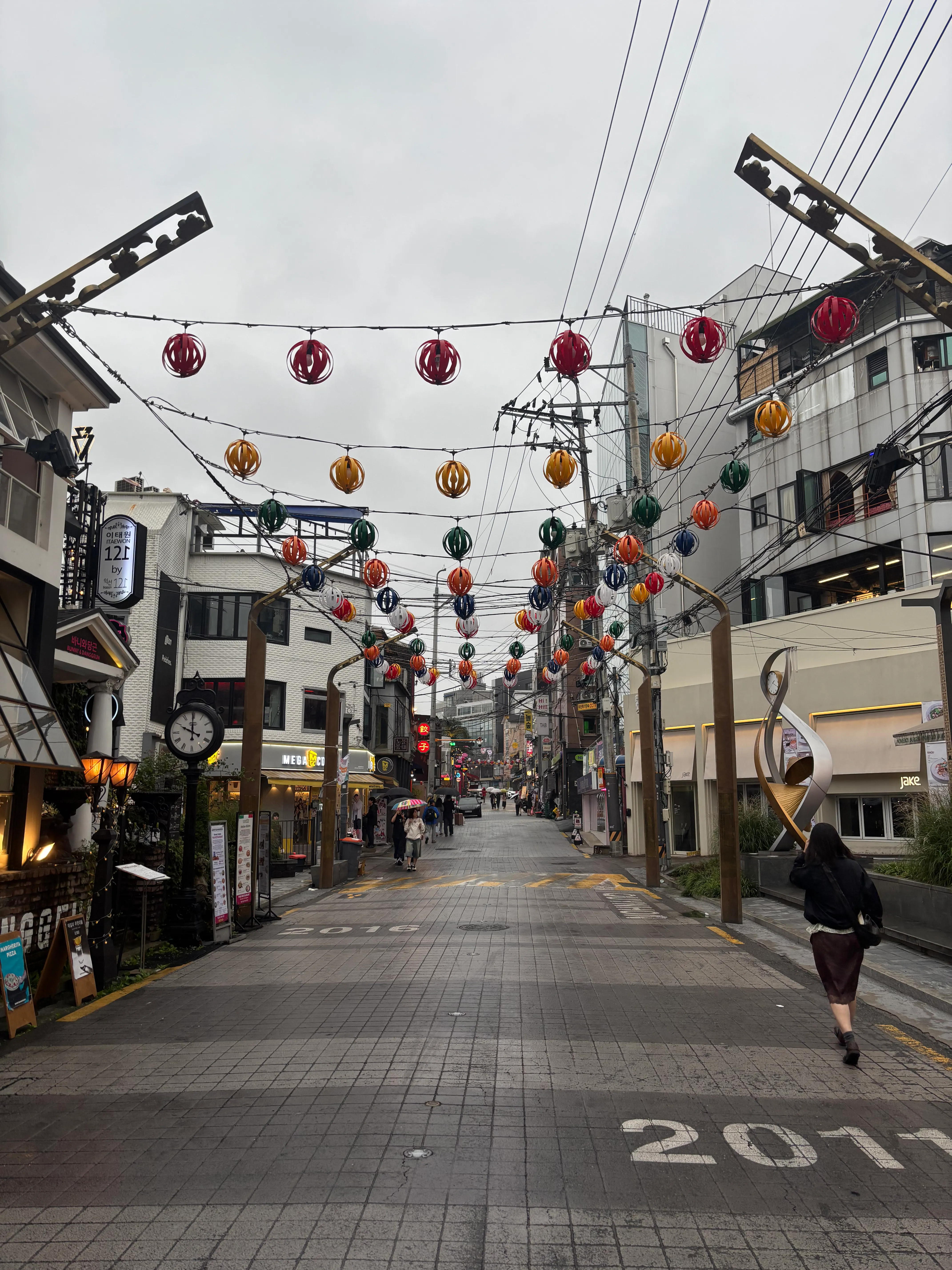 A covered shopping street decorated with colorful hanging paper lanterns in red, orange, yellow, green, and blue strung across overhead lines