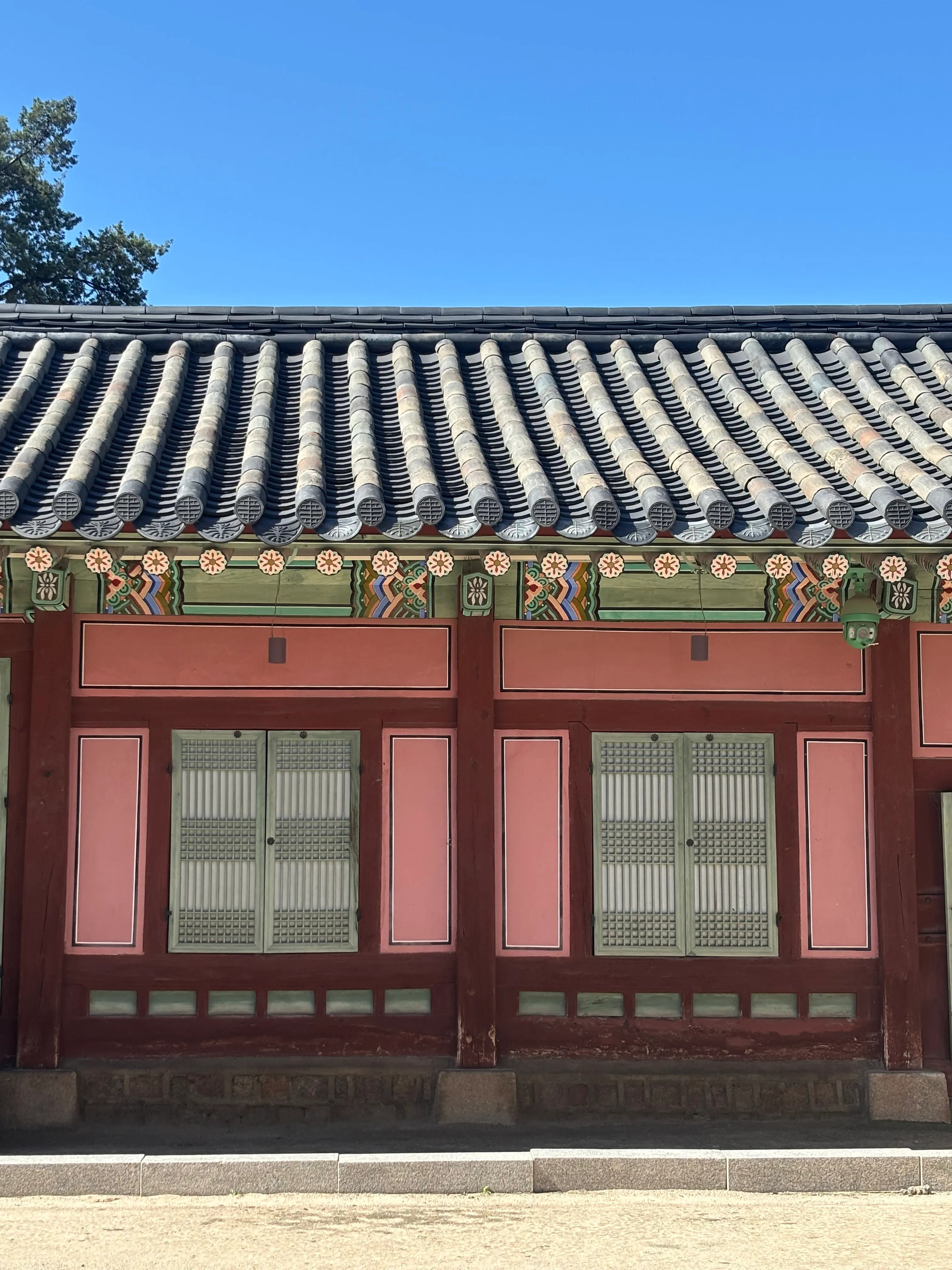 Face of a building with pink walls, rectangles with white and black borders, and intricate, colorful designs, found at Gyeongbokgung Palace in Seoul, Korea