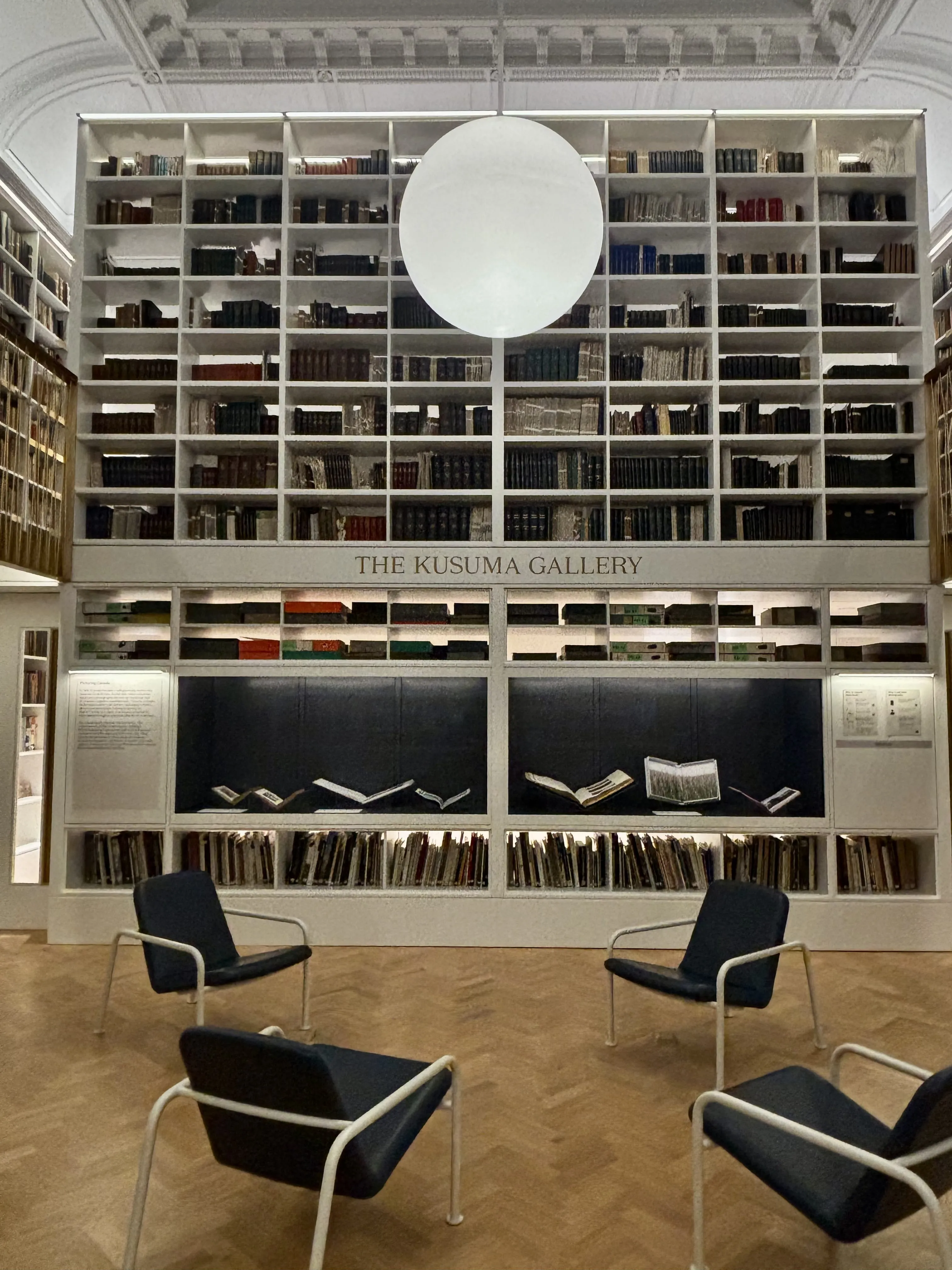 Four empty chairs in front of a large, grid-shaped bookcase full of books in the The Kusuma Gallery at Tate Modern