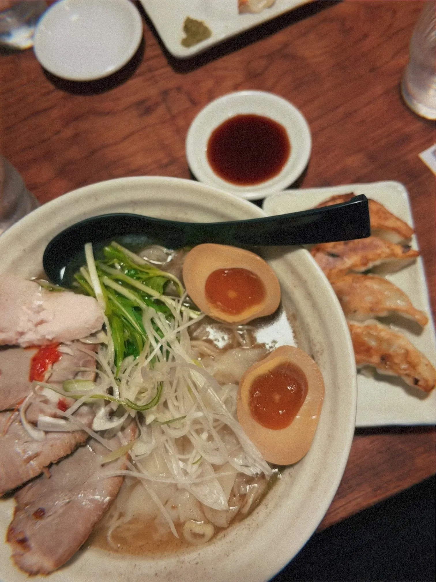 Aerial view of ramen with noodles, egg, pork, and green onion. Accompanied by crispy dumplings