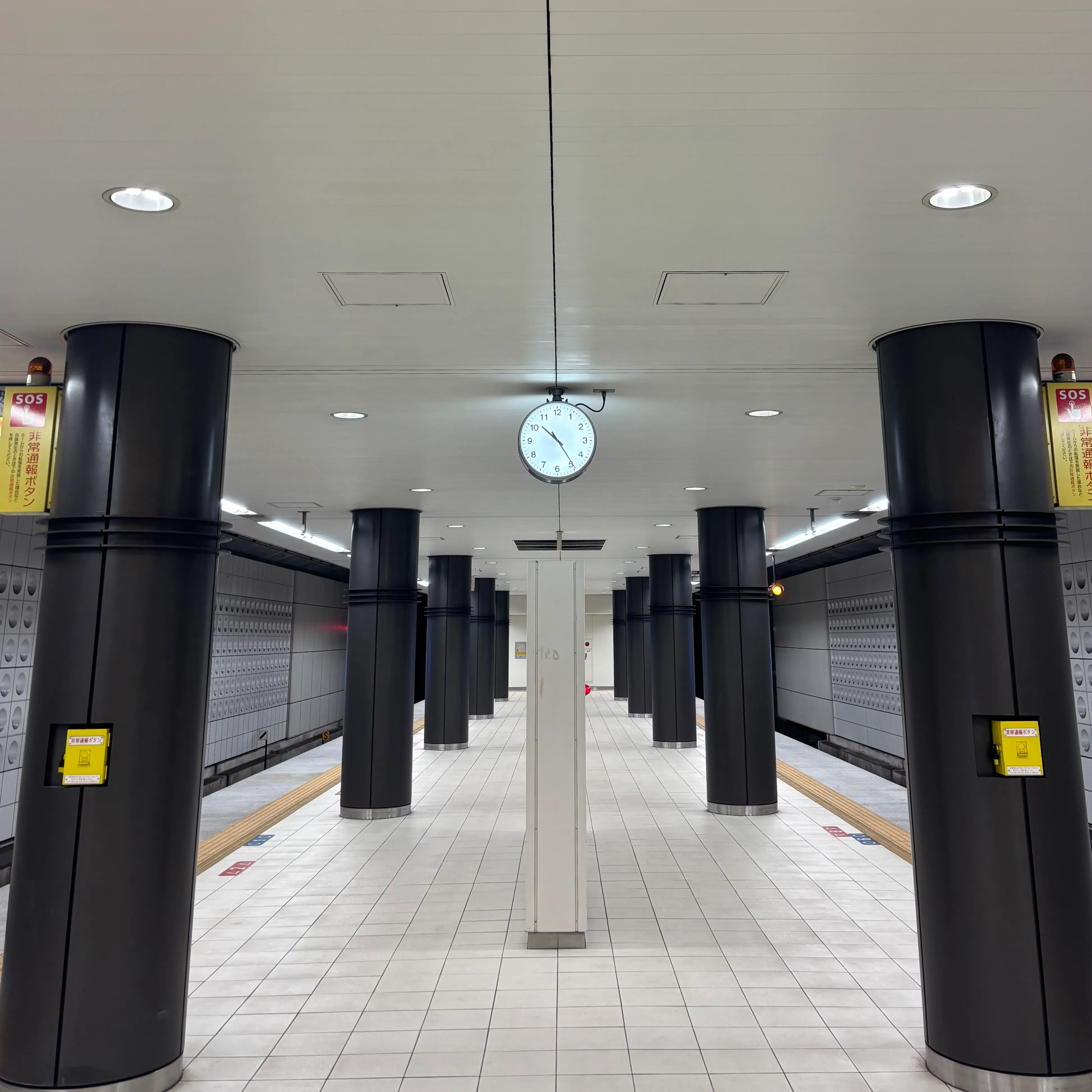 A train station in Osaka, Japan with a white pillar and an analog clock in the center, displaying 10:25 PM, surrounded by symmetrical pillars on both sides