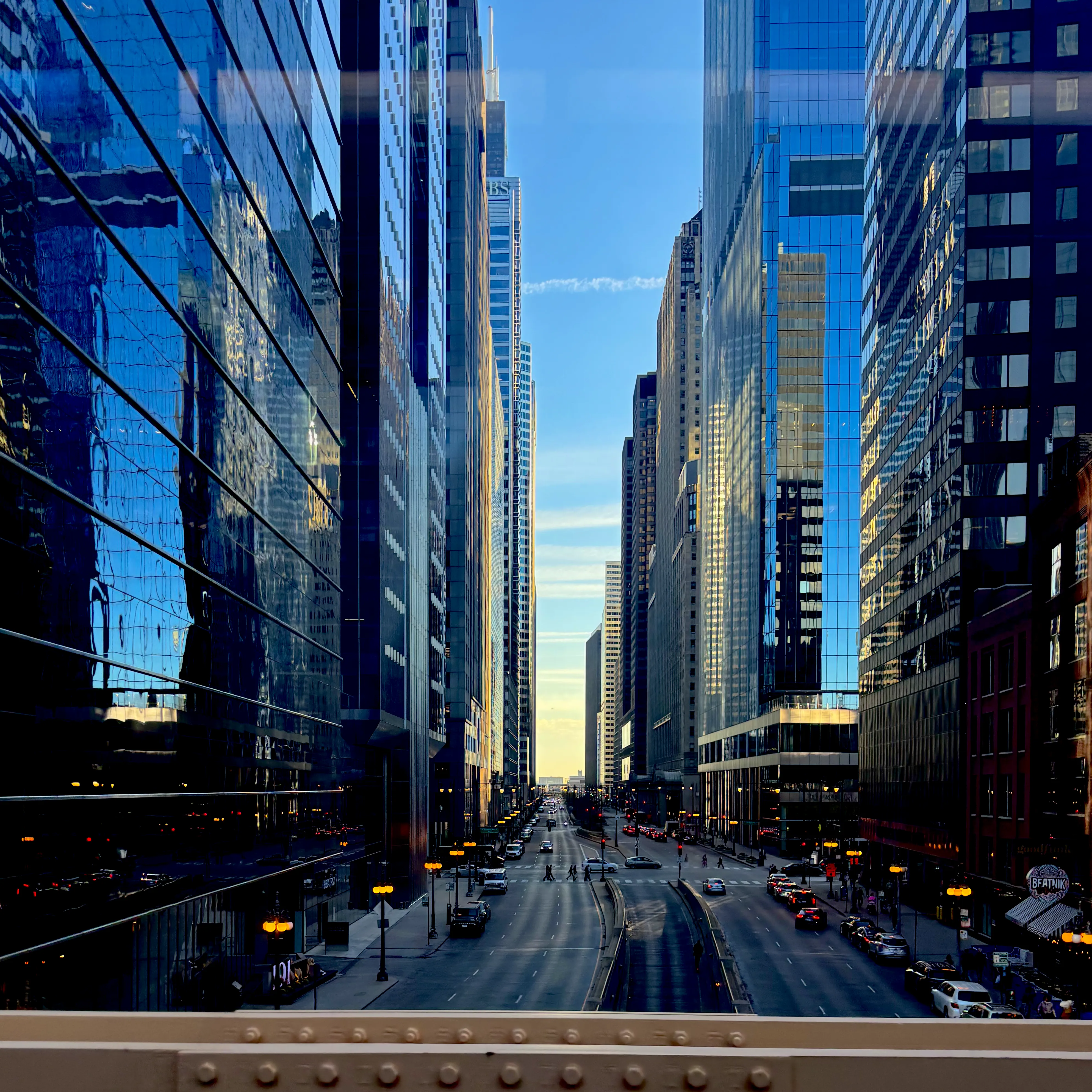 Wacker Drive in Chicago at golden hour, with towering glass skyscrapers lining both sides of the wide boulevard under a blue sky with warm sunset lighting
